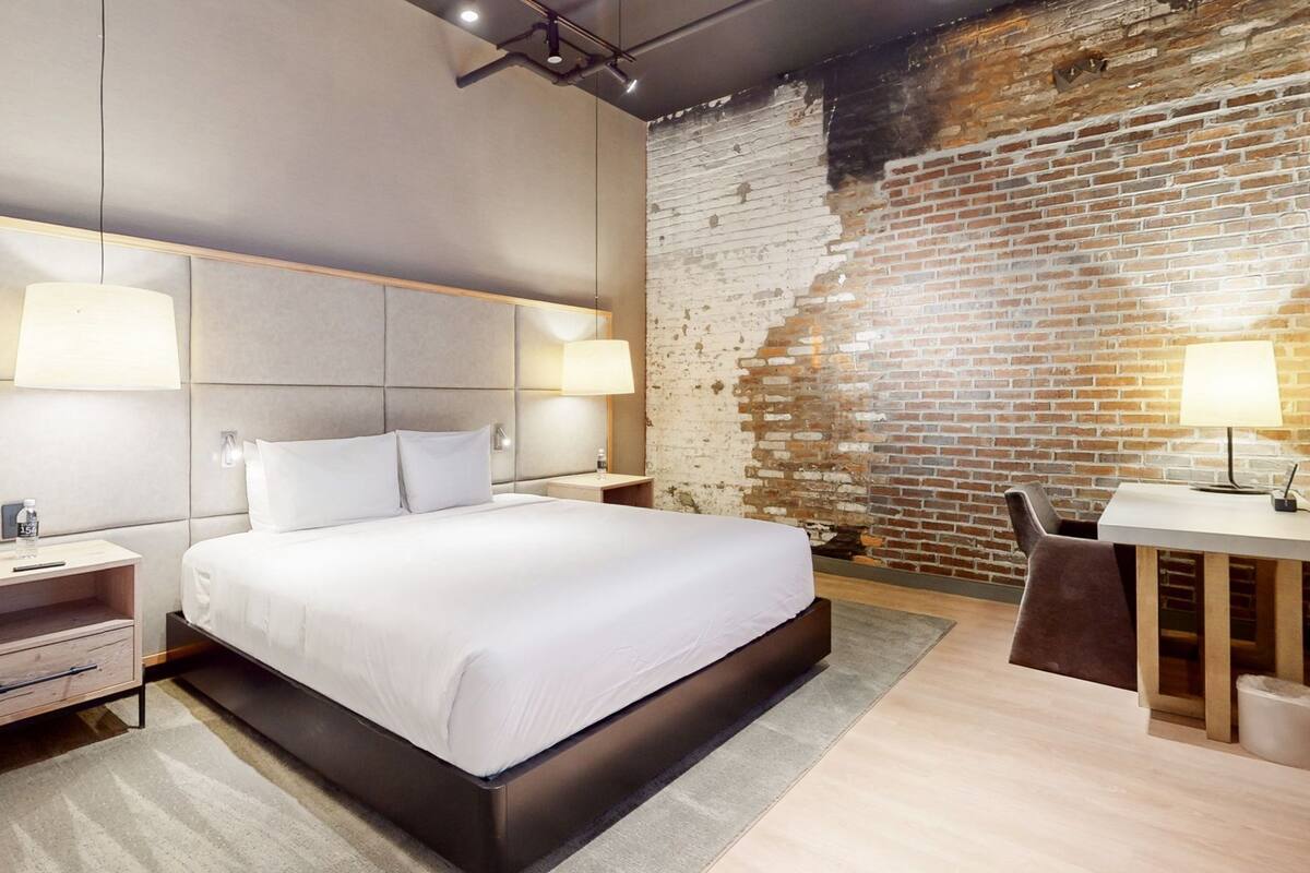 A modern hotel room with a large bed, a desk, and a brick wall.