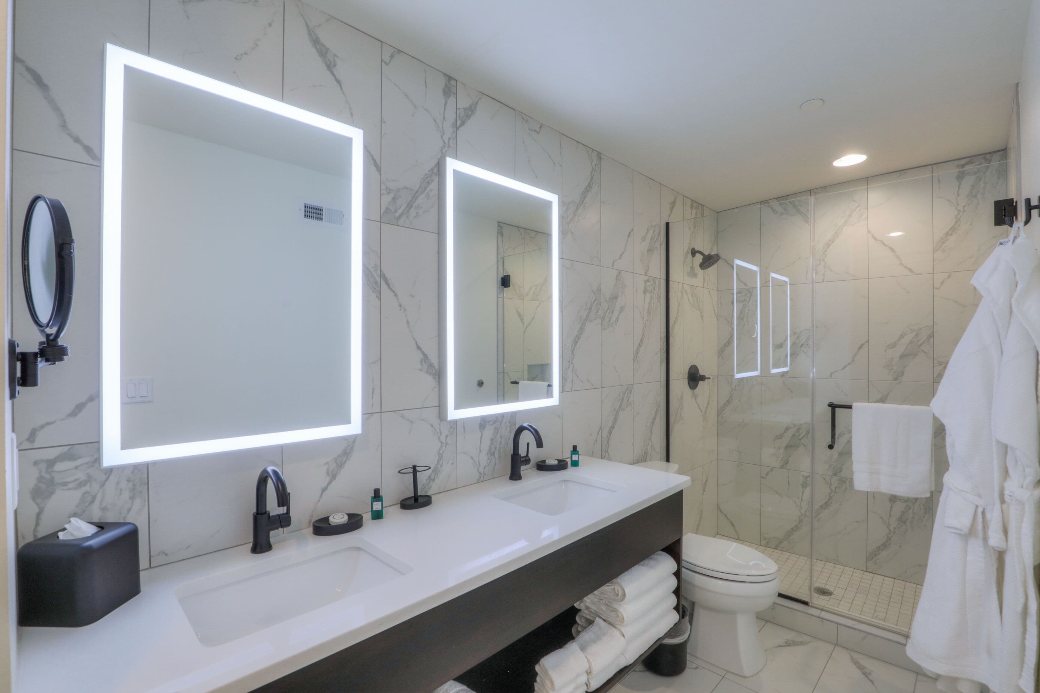 A modern bathroom with two sinks, a large mirror, and a shower area.