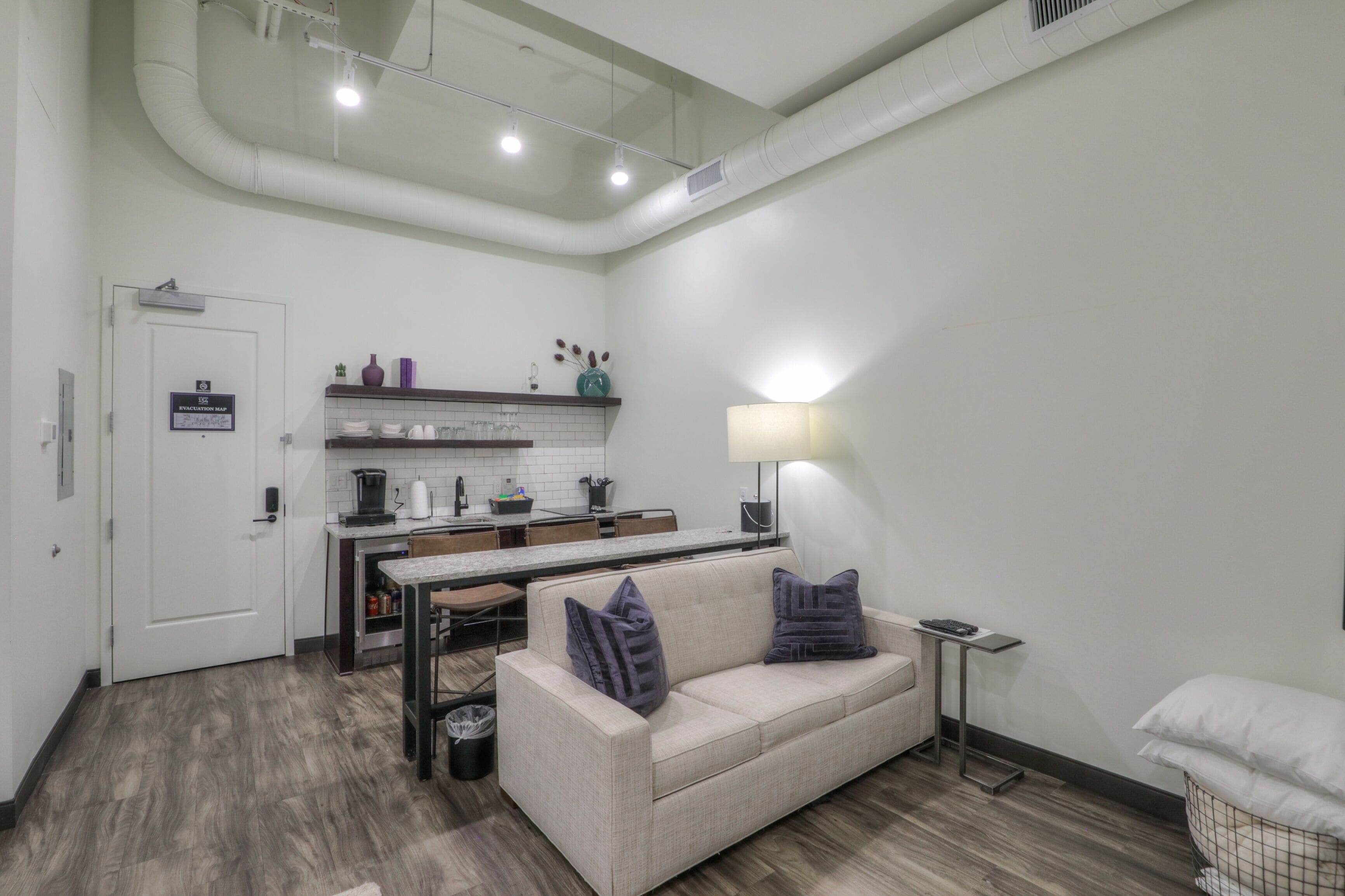 Un espace de vie compact comprenant un coin cuisine, un canapé avec des coussins, une petite table et une lampe.