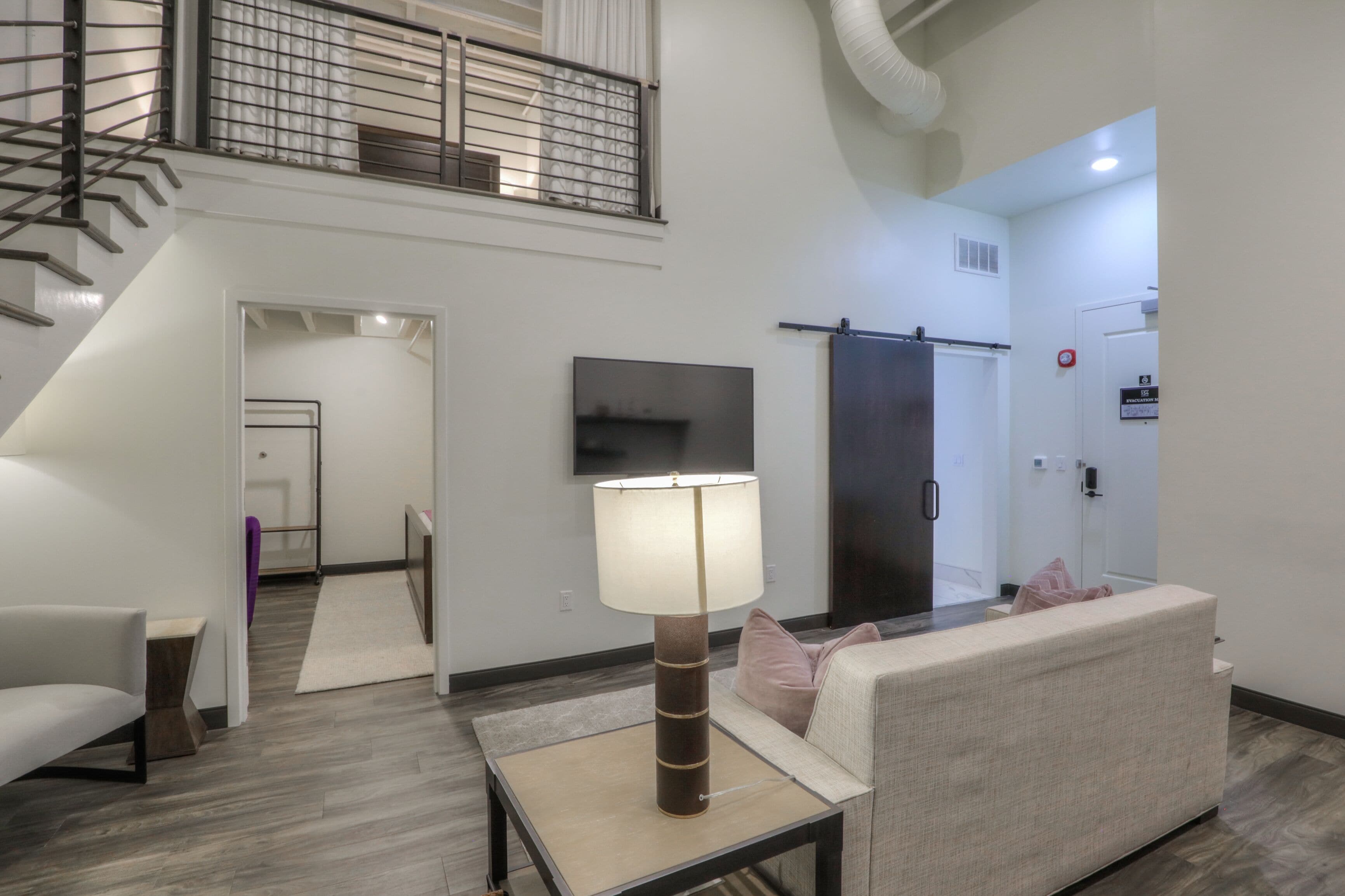 A modern living room with a sofa, a table with a lamp, a TV, and a staircase.