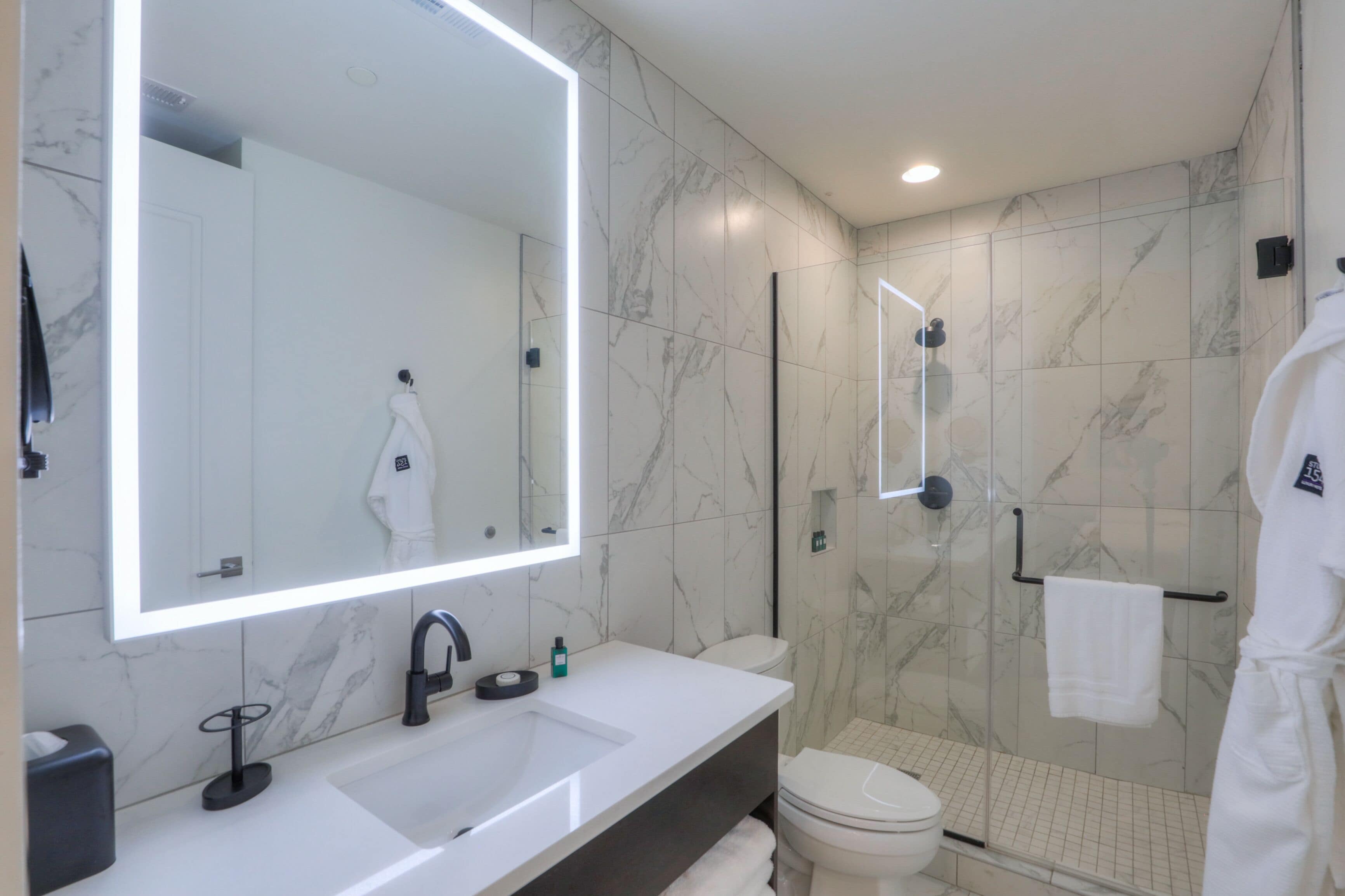 A modern bathroom with a large mirror, a sink, a toilet, and a shower area.
