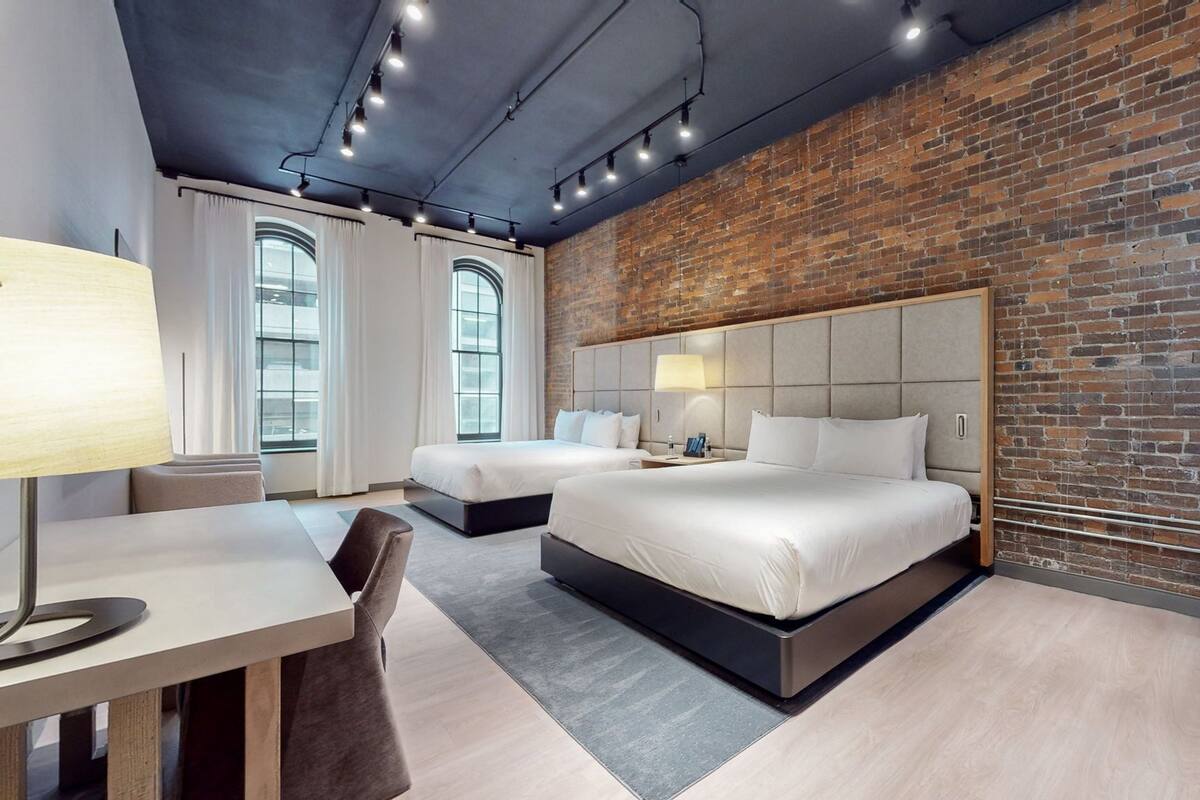 A modern hotel room with two beds, a desk, and a large window.