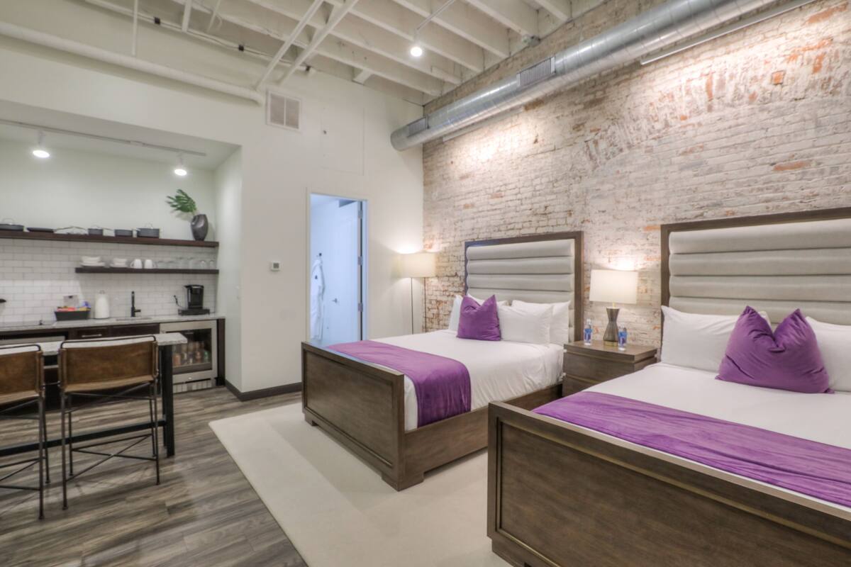 A hotel room with two beds, a kitchenette, and a dining area.