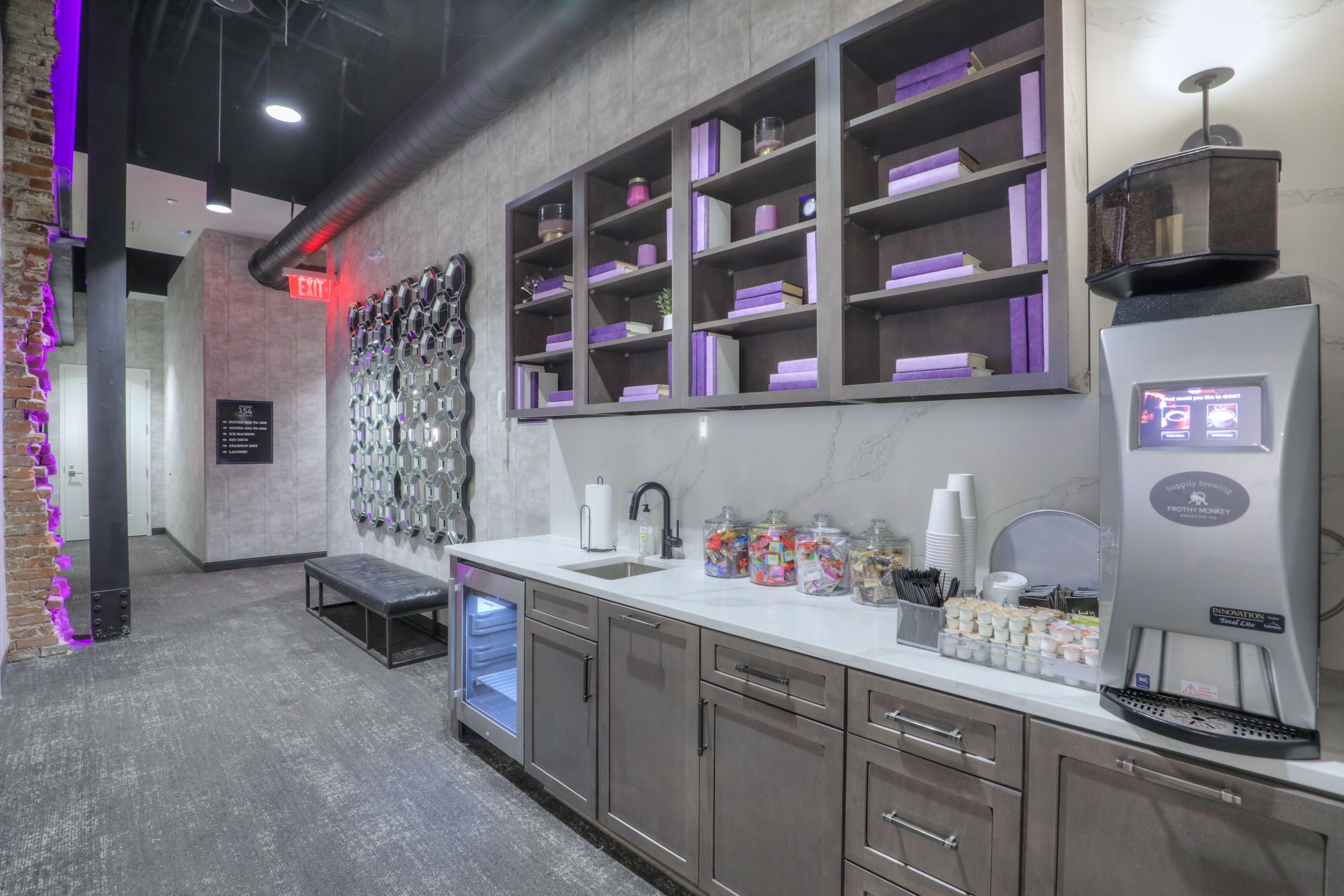 A modern kitchen with a built-in espresso machine, a coffee station, and a wall-mounted shelf with books and decorative items.