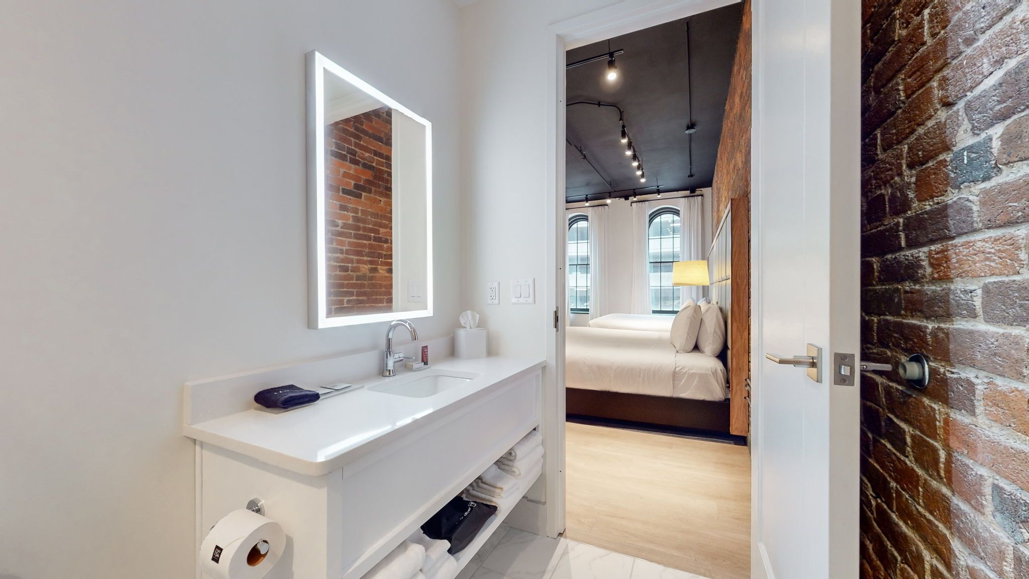 A modern bathroom with a white vanity, a large mirror, and a visible brick wall.
