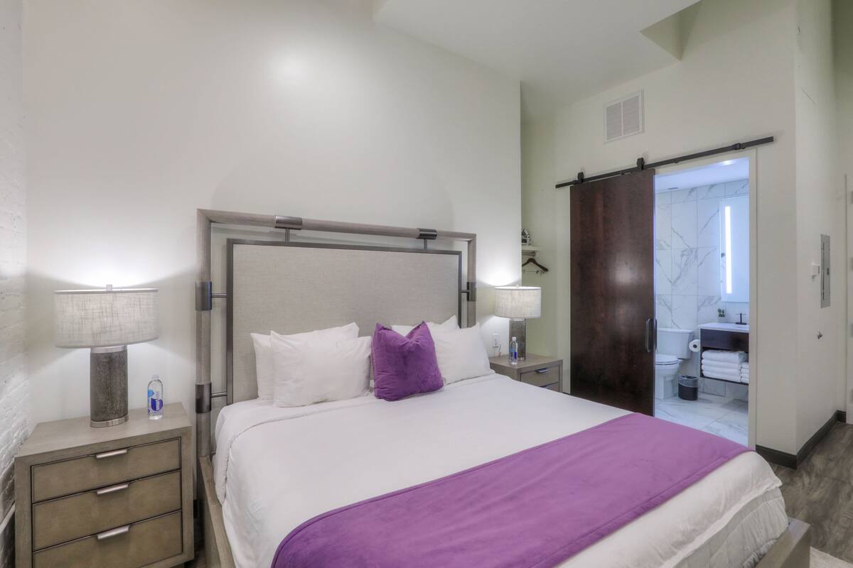 A hotel room with a bed, nightstands, a bathroom visible through an open door, and a towel rack.