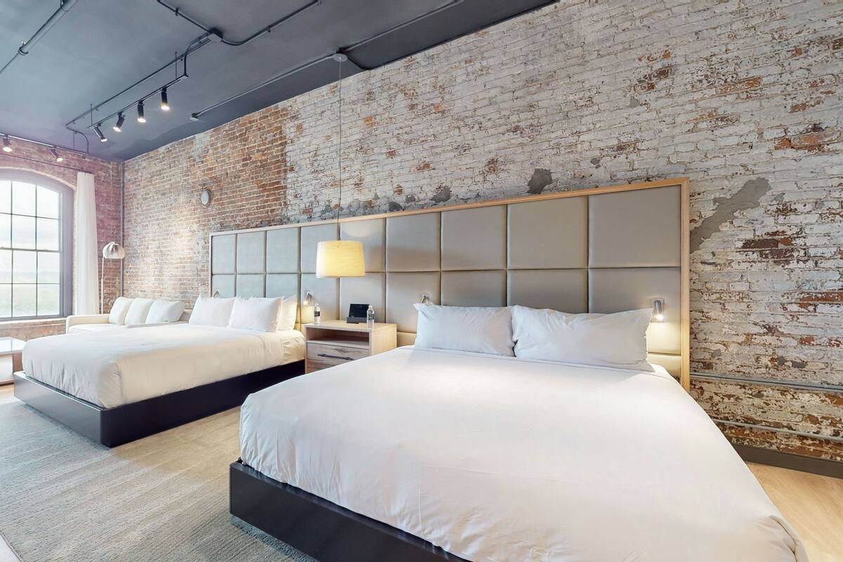 A hotel room with two beds, a brick wall, and a large window.