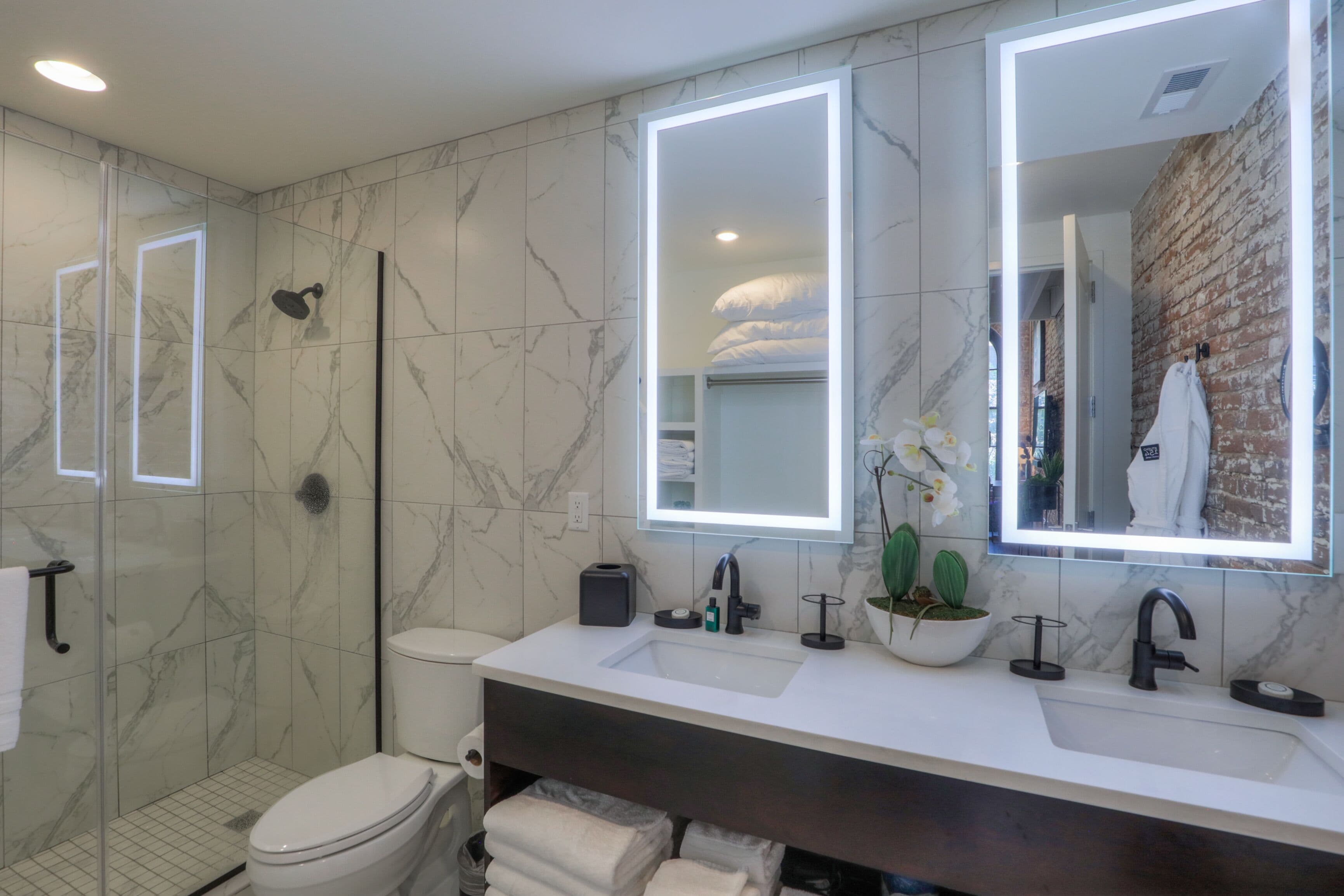 A modern bathroom with a marble floor, a white sink with a dark countertop, a large mirror, and a shower enclosure.