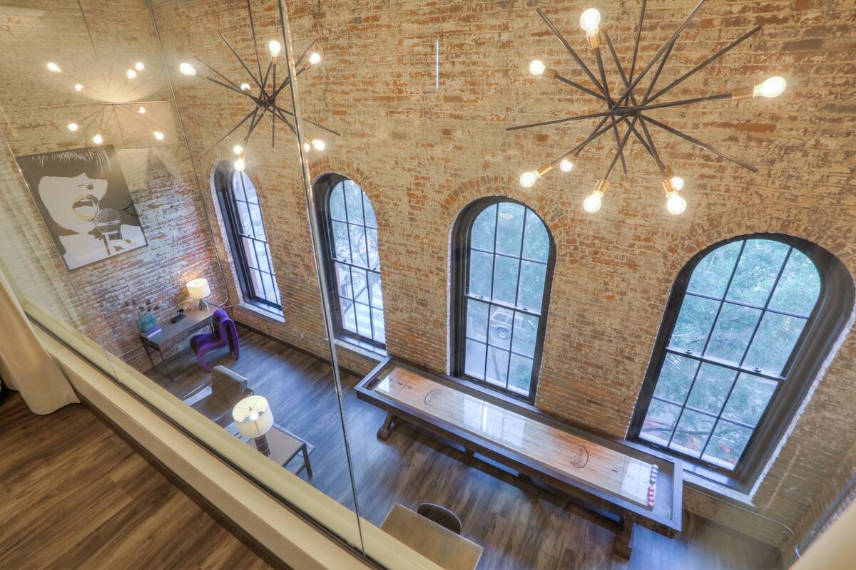 A spacious room with large arched windows, a long wooden table, and a modern chandelier.