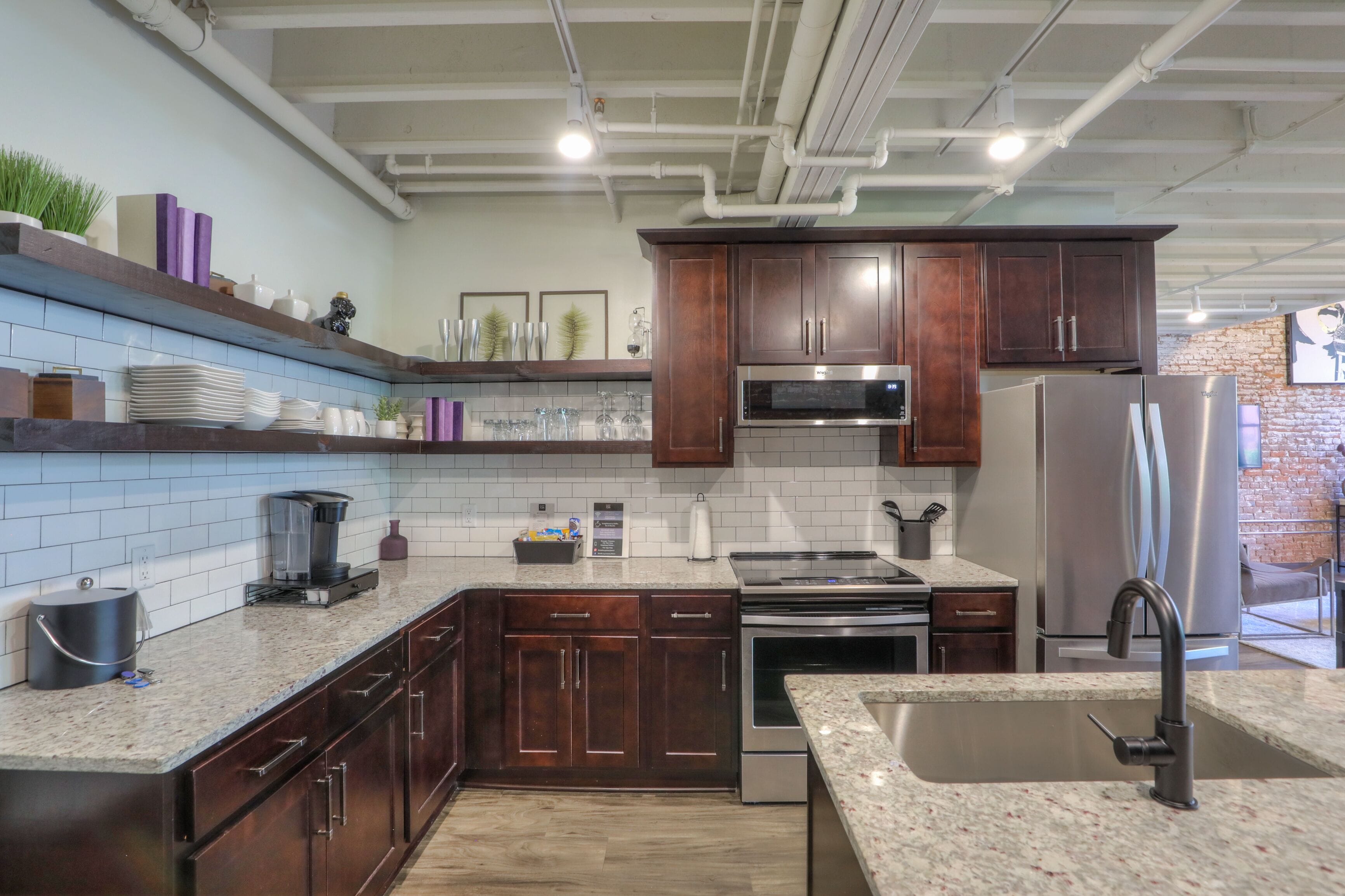 A modern kitchen with dark wooden cabinets, a stainless steel refrigerator, a built-in oven, and a granite countertop.