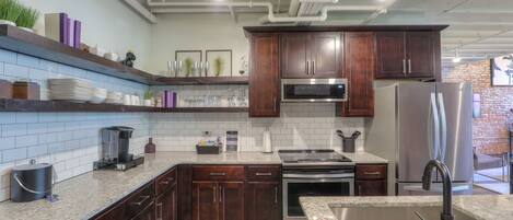 A modern kitchen with dark wooden cabinets, a stainless steel refrigerator, a built-in oven, and a granite countertop.