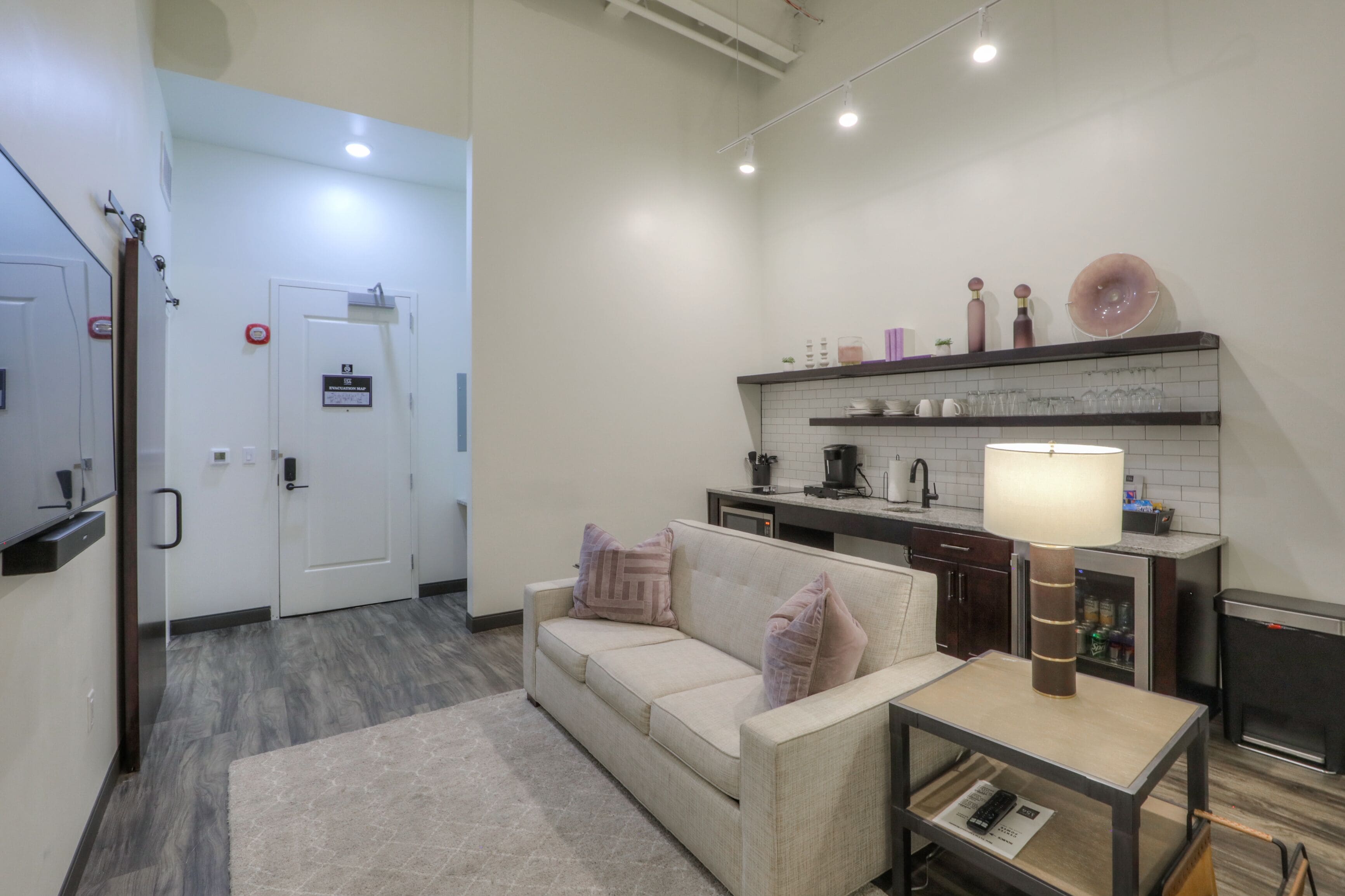 A modern kitchen with a white countertop, a built-in stove, and a coffee machine. There is a beige sofa with a rug in front of it.