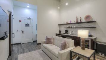 A modern kitchen with a white countertop, a built-in stove, and a coffee machine. There is a beige sofa with a rug in front of it.