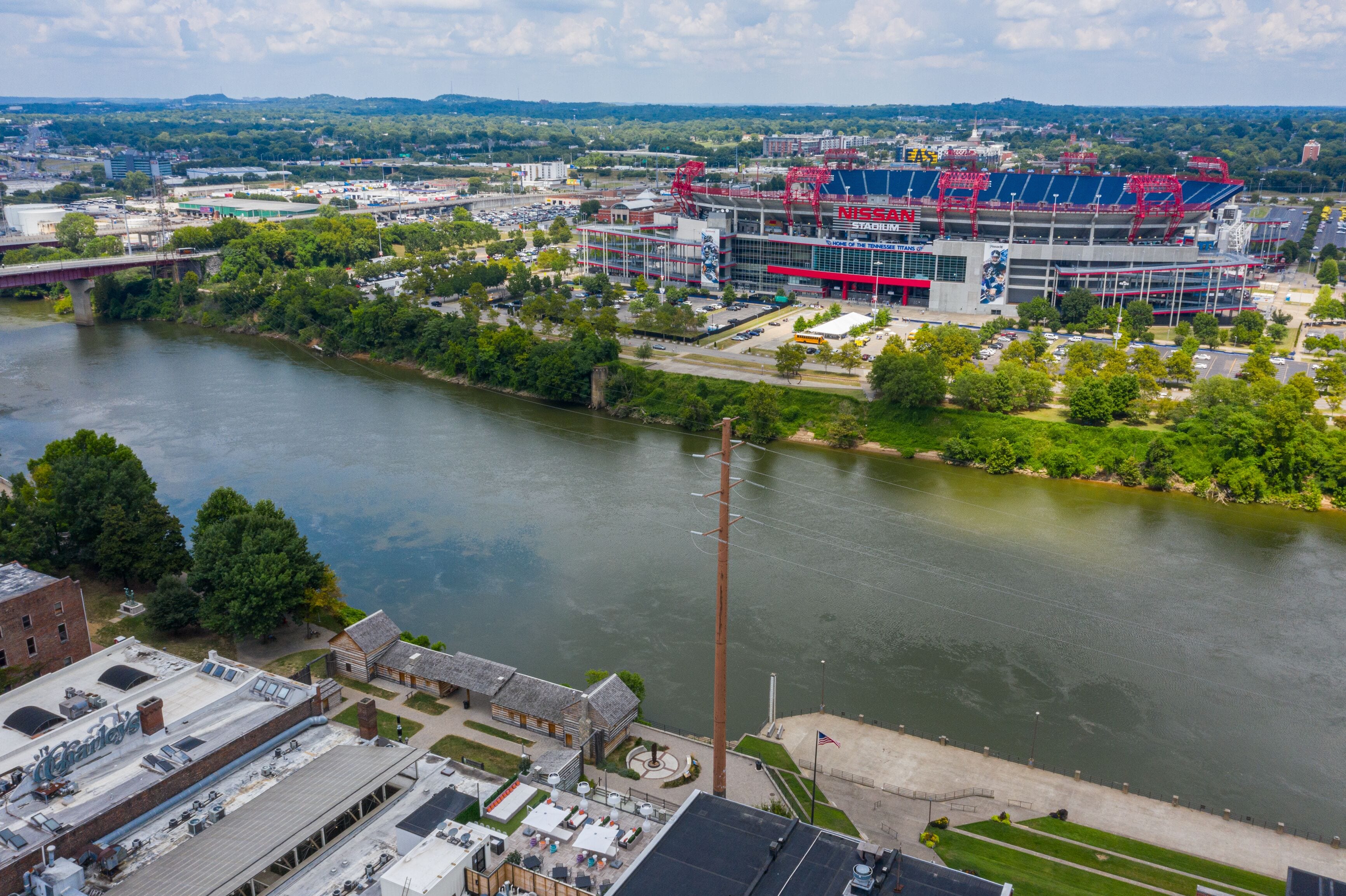A stadium with a river in the foreground, surrounded by greenery and buildings.