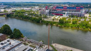 A stadium with a river in the foreground, surrounded by greenery and buildings.