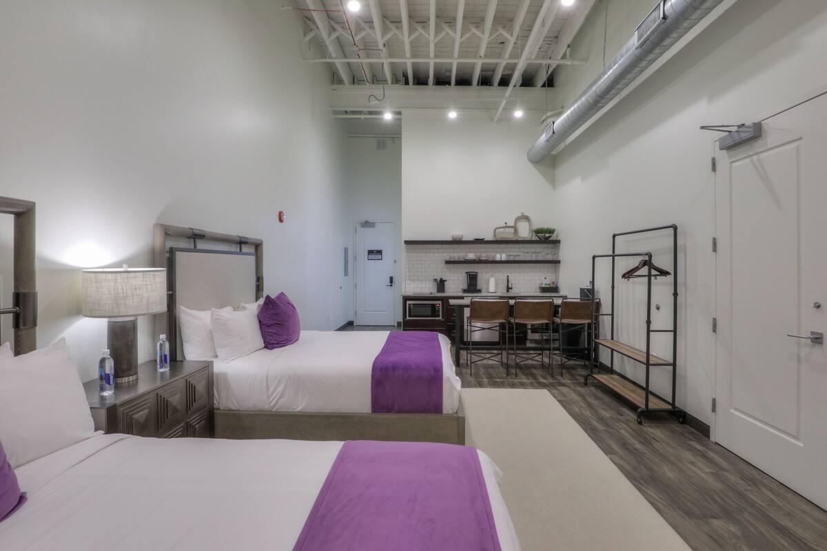 A hotel room with two beds, a desk, and a kitchenette.