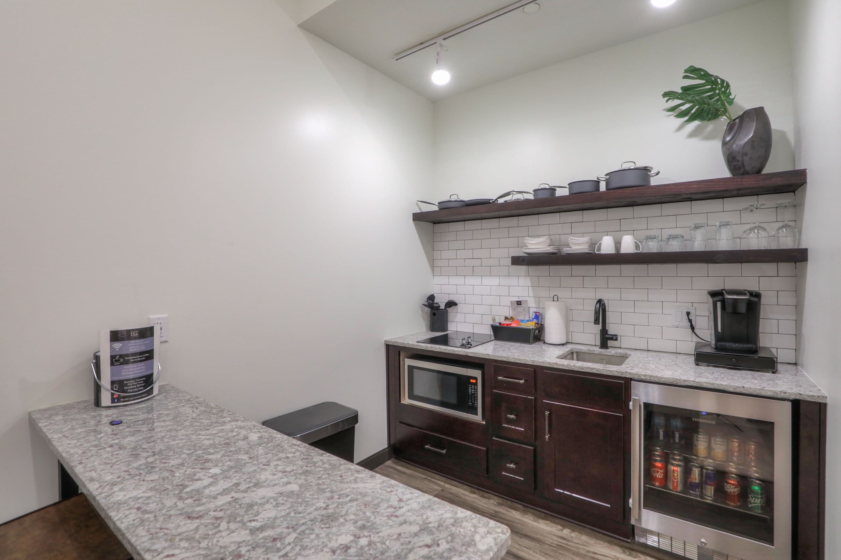 A modern kitchen with a granite countertop, a built-in microwave, a coffee maker, and a refrigerator with a beverage dispenser.