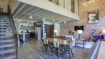 Una cocina amplia con una isla central, un comedor con una mesa y sillas de madera, y una escalera que sube a un nivel superior.