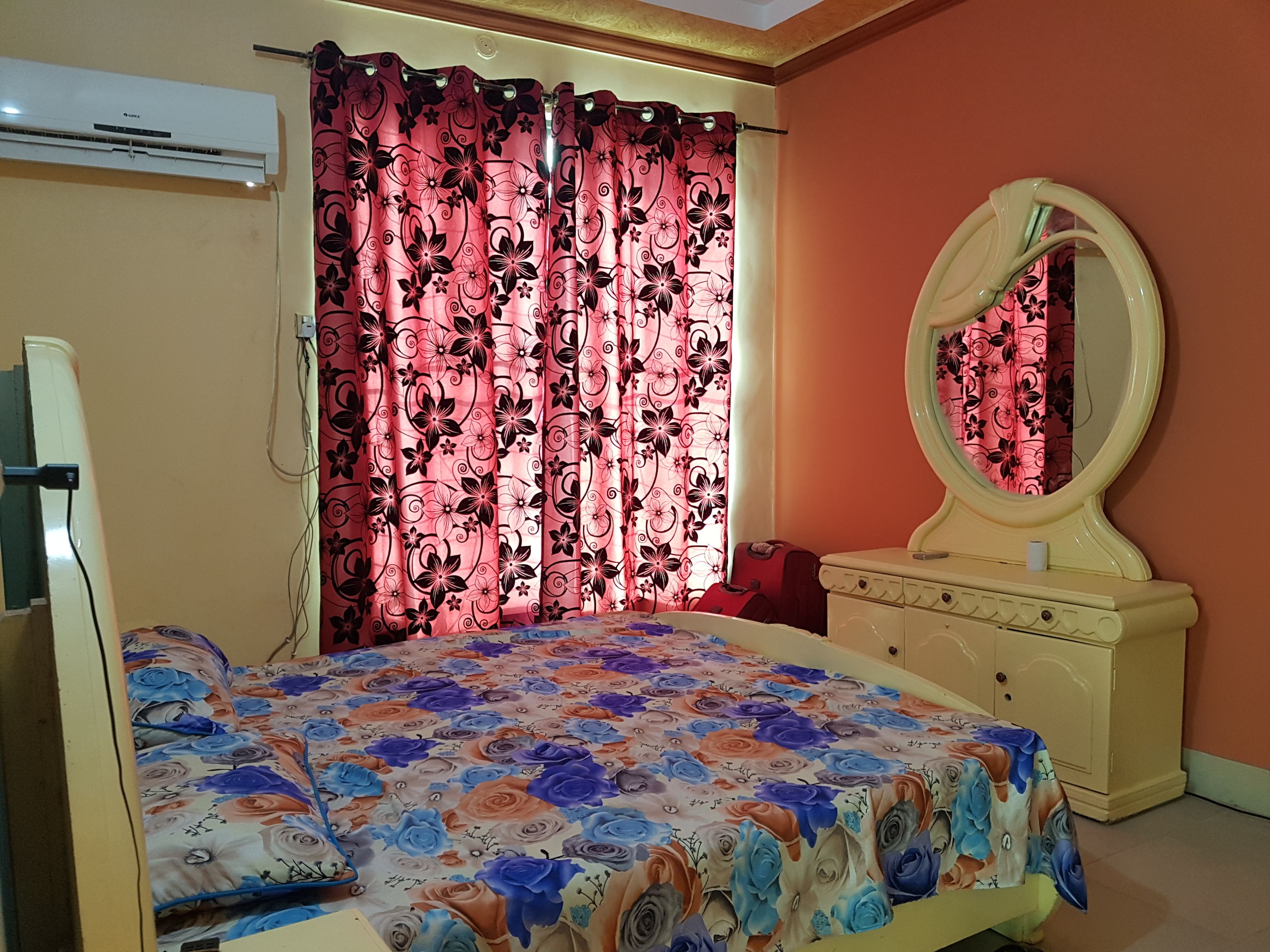 A bedroom with a bed, a vanity with a mirror, and a window with curtains.
