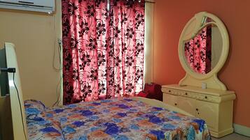 A bedroom with a bed, a vanity with a mirror, and a window with curtains.
