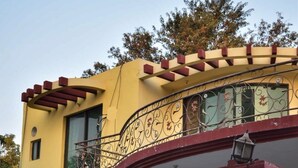 Ein zweistöckiges Haus mit gelber Fassade, einem braunen Tor und einem geparkten Auto davor.
