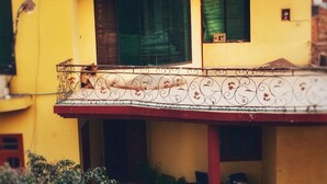 Ein gelbes Gebäude mit einem Balkon, einem Fenster mit Metallgitter und einer kleinen Tür.