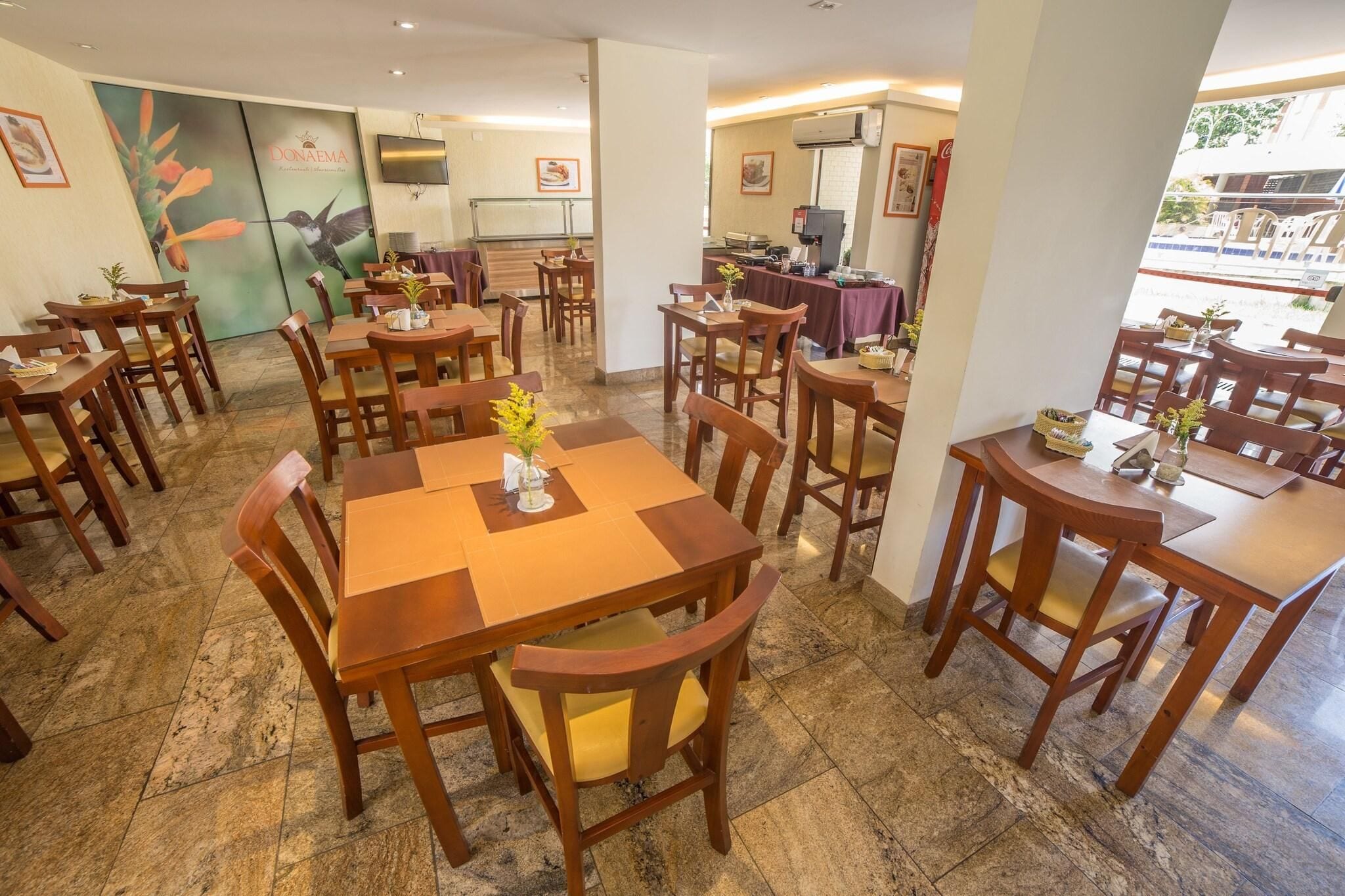 A restaurant with multiple wooden tables and chairs, a tiled floor, and a large painting on the wall.