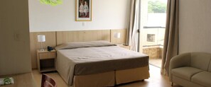 A hotel room with a bed, bedside tables, a chair, and a window with curtains. - Ema Palace (São José dos Campos)