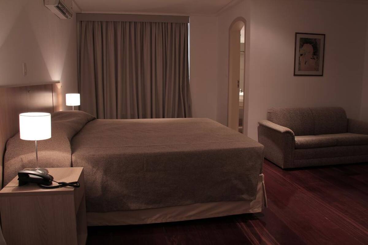 A hotel room with a large bed, a bedside lamp, a chair, and a painting on the wall.