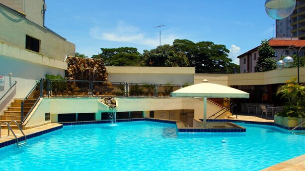 Ein Swimmingpool mit Wasserfall, Treppen zu einem überdachten Bereich und Sitzgelegenheiten im Freien.