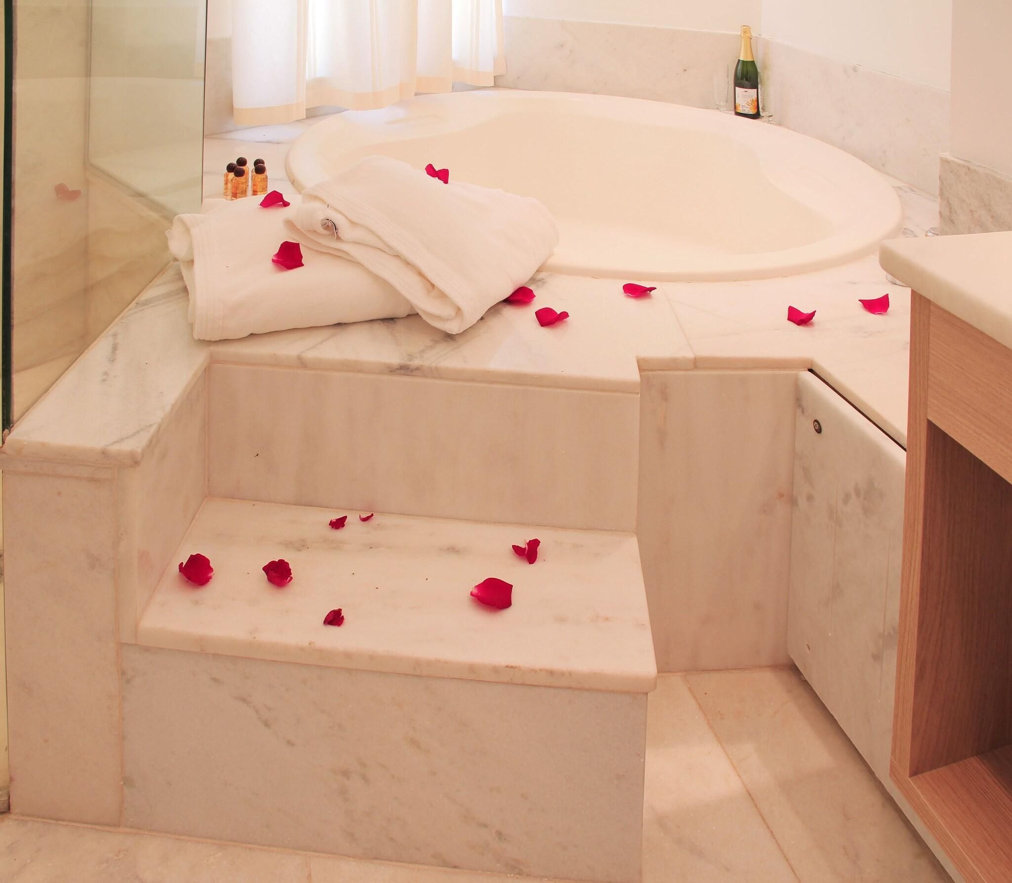 A bathroom with a marble tub, steps, and rose petals.