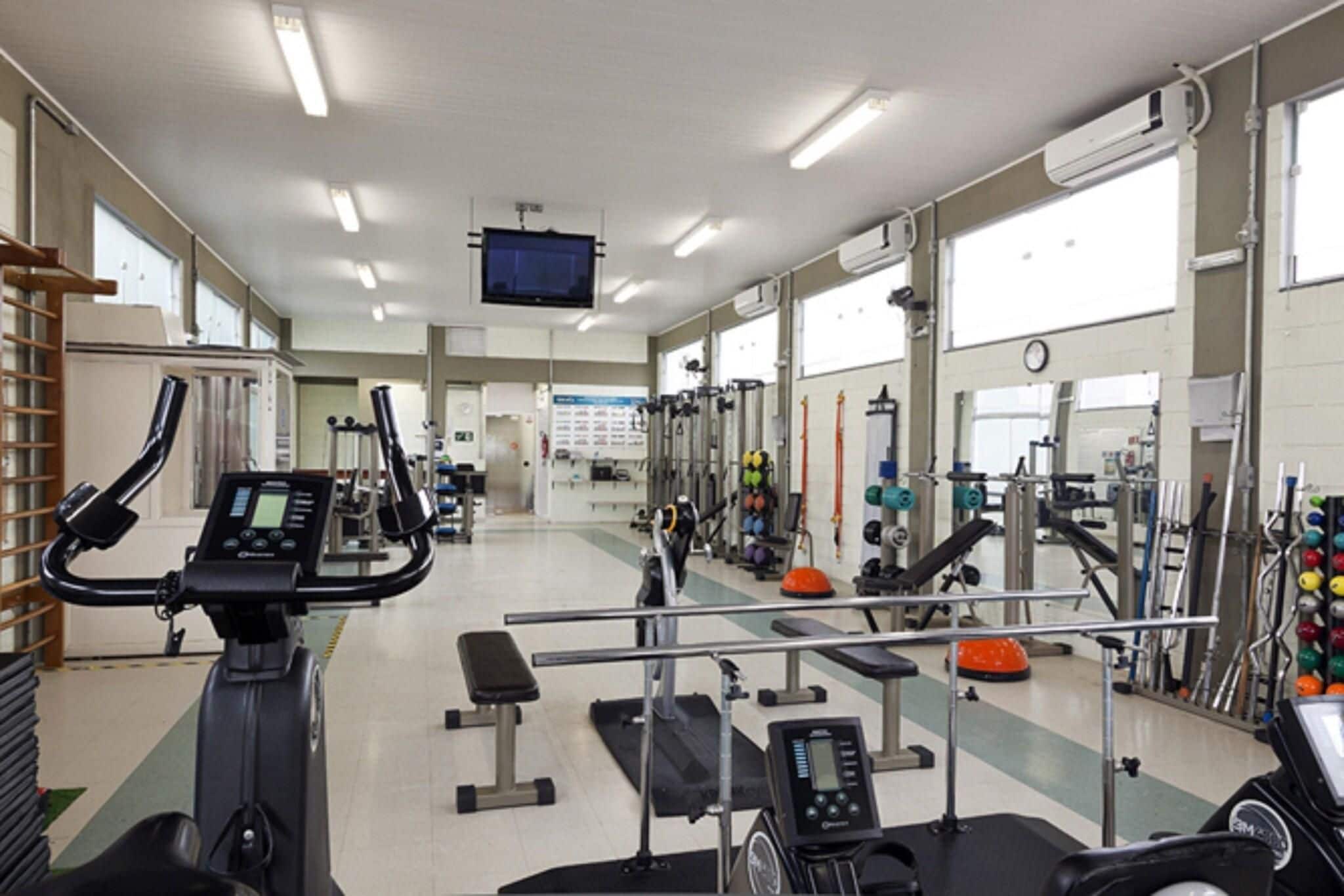 A gym with various exercise equipment, a television screen, and large windows.