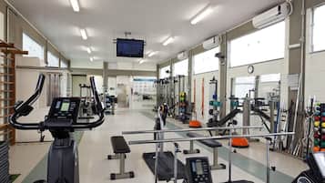 A gym with various exercise equipment, a television screen, and large windows.