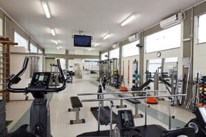 A gym with various exercise equipment, a television screen, and large windows.