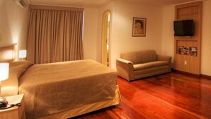 Ein Hotelzimmer mit einem großen Bett, einer Couch, einem Fernseher und einem Holzschrank.