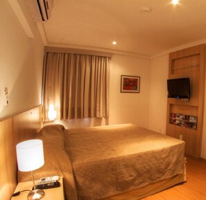 A hotel room with a bed, a TV, a lamp, and a painting on the wall.