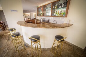A bar area with a granite countertop, bar stools, and a glass display case with bottles. - Ema Palace (São José dos Campos)