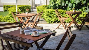 Sitzgelegenheiten im Freien mit Tischen und Stühlen, ein Blumentopf und eine Zeitung.