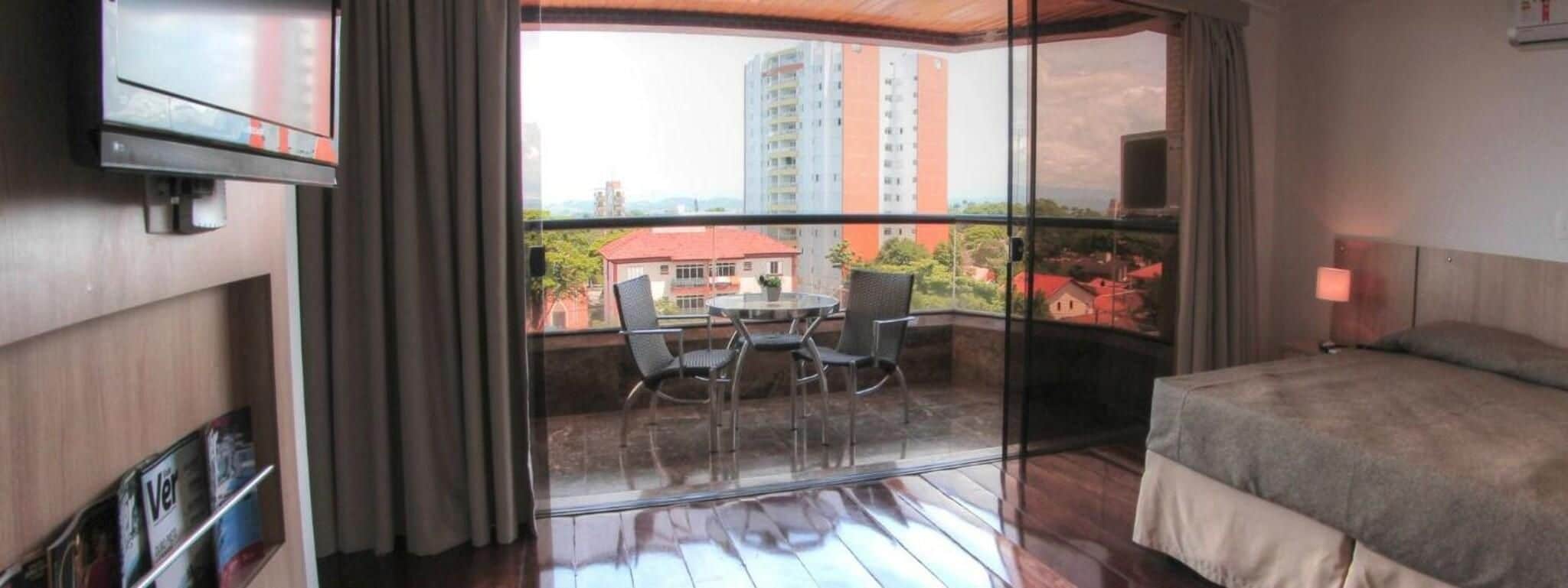 Habitación de hotel con balcón, cama, televisor y mesa con sillas.