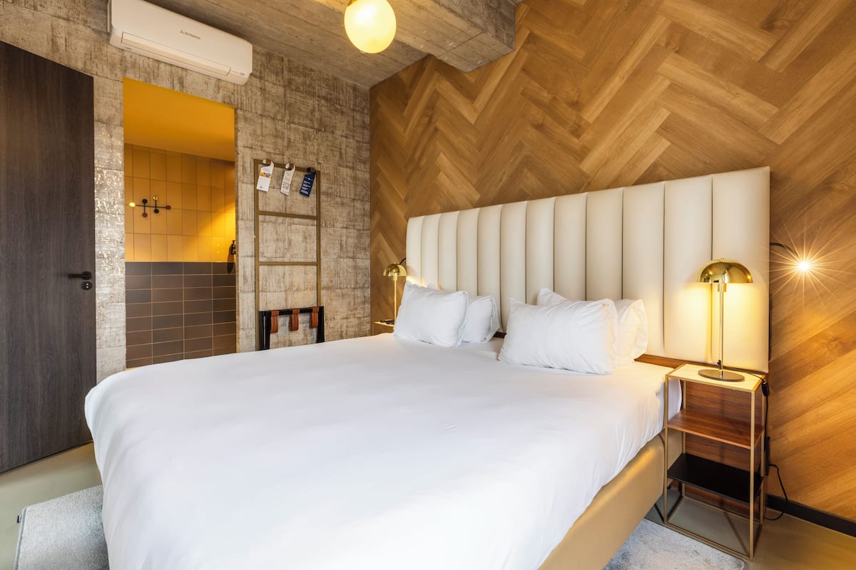 Une chambre d’hôtel avec un grand lit, des murs en bois, une étagère intégrée et un climatiseur fixé au mur.