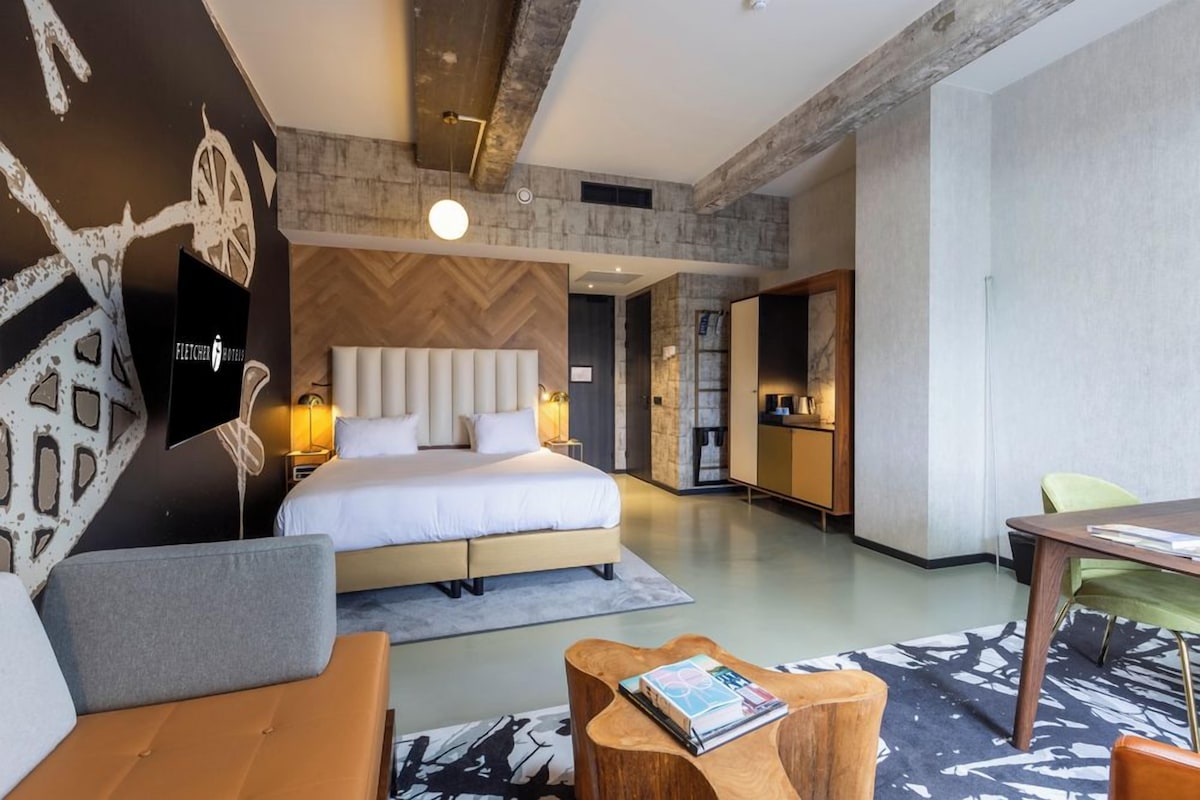 Une chambre d’hôtel moderne avec un grand lit, un canapé, une table basse en bois et un coin repas.