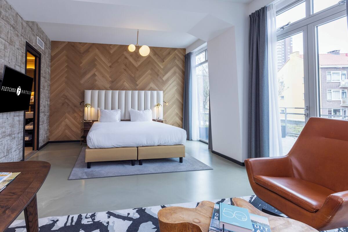 Une chambre d’hôtel moderne dotée d’un grand lit, d’une télévision et offrant une vue sur la ville grâce à de grandes fenêtres.
