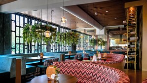 Un restaurante con cabinas y mesas, plantas colgantes y una estantería para vinos.