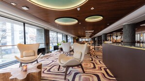 Un vestíbulo moderno con alfombra de diseño geométrico, sillas contemporáneas y un techo de madera con iluminación circular.