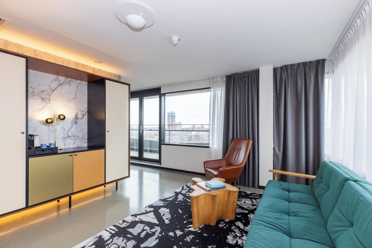 Un salon moderne comprenant un canapé, une table basse, un fauteuil et un coin cuisine avec un revêtement mural en marbre.