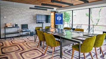 A modern conference room with a large table, yellow chairs, a TV, and a 'Welcome' banner.