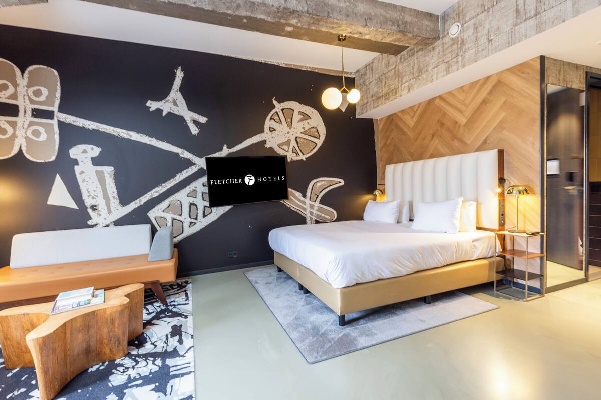 Une chambre d’hôtel moderne dotée d’un grand lit, d’une tête de lit en bois, d’un téléviseur fixé au mur et d’une fresque murale originale en noir et blanc.