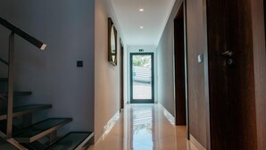 A modern hotel hallway with a glass staircase, a wooden door, and a view of the outside. - Mediterranean Villas (Santa Cruz)
