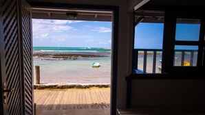 An open door leading to a beach view with a wooden deck and a doormat.