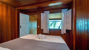 A wooden-paneled bedroom with a bed, two white doors, and a window with curtains.